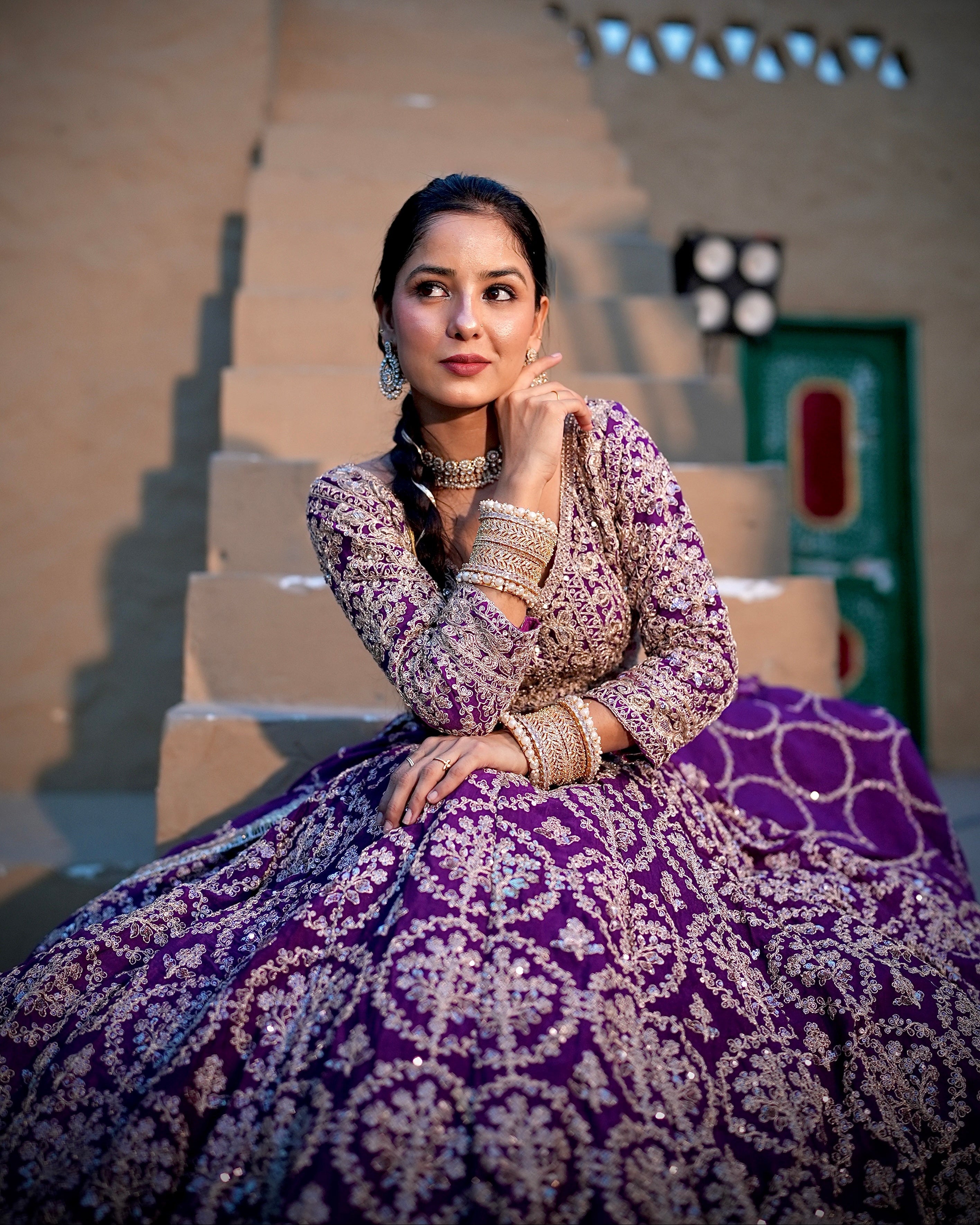 Woman in a purple and white traditional outfit sitting on steps outdoors.