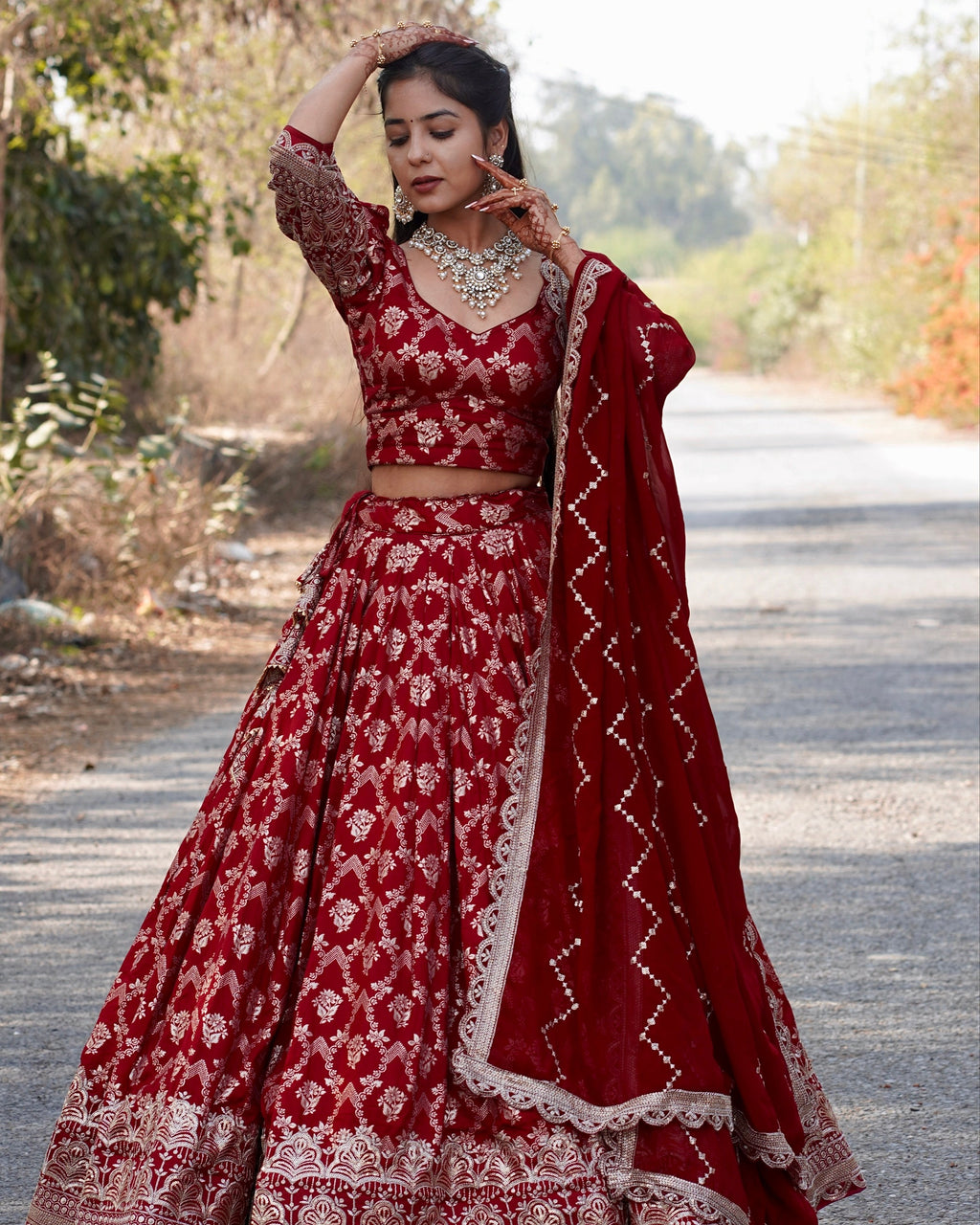 Woman in a red and white traditional outfit standing outdoors with trees in the background