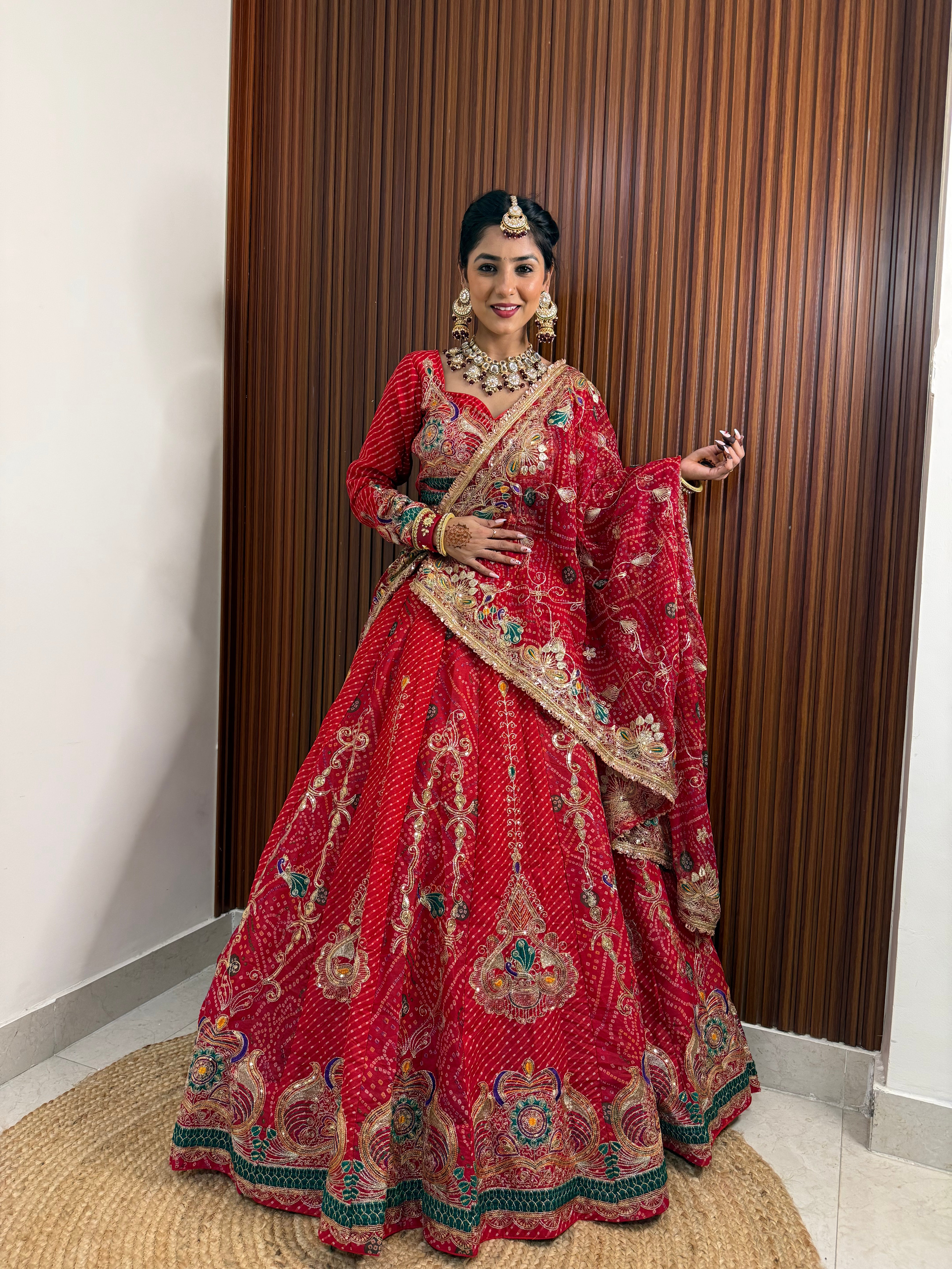 Woman in a red traditional outfit with intricate patterns standing against a wooden panel background.