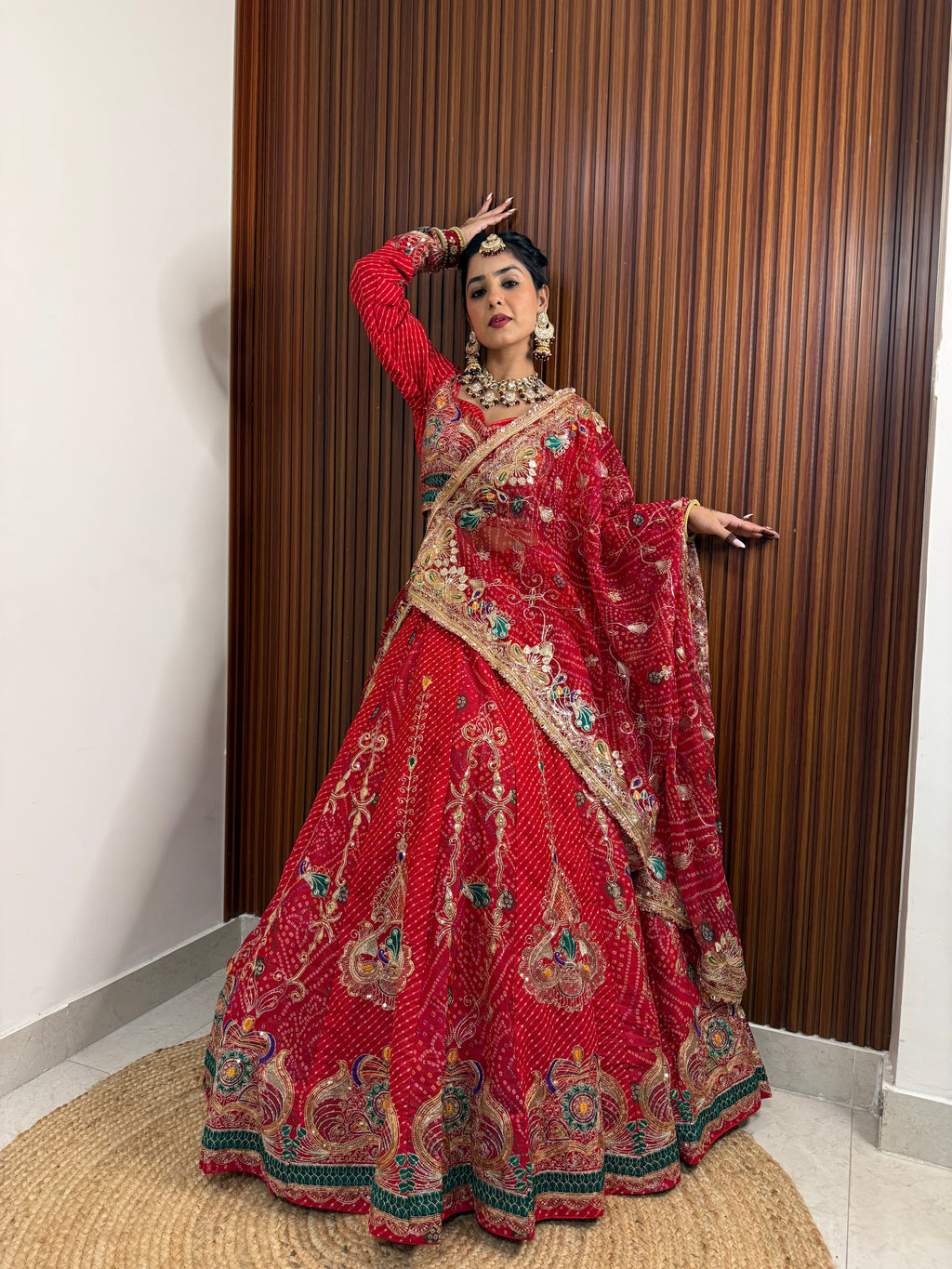 Woman in a traditional red and gold embroidered outfit standing against a wooden paneled wall.