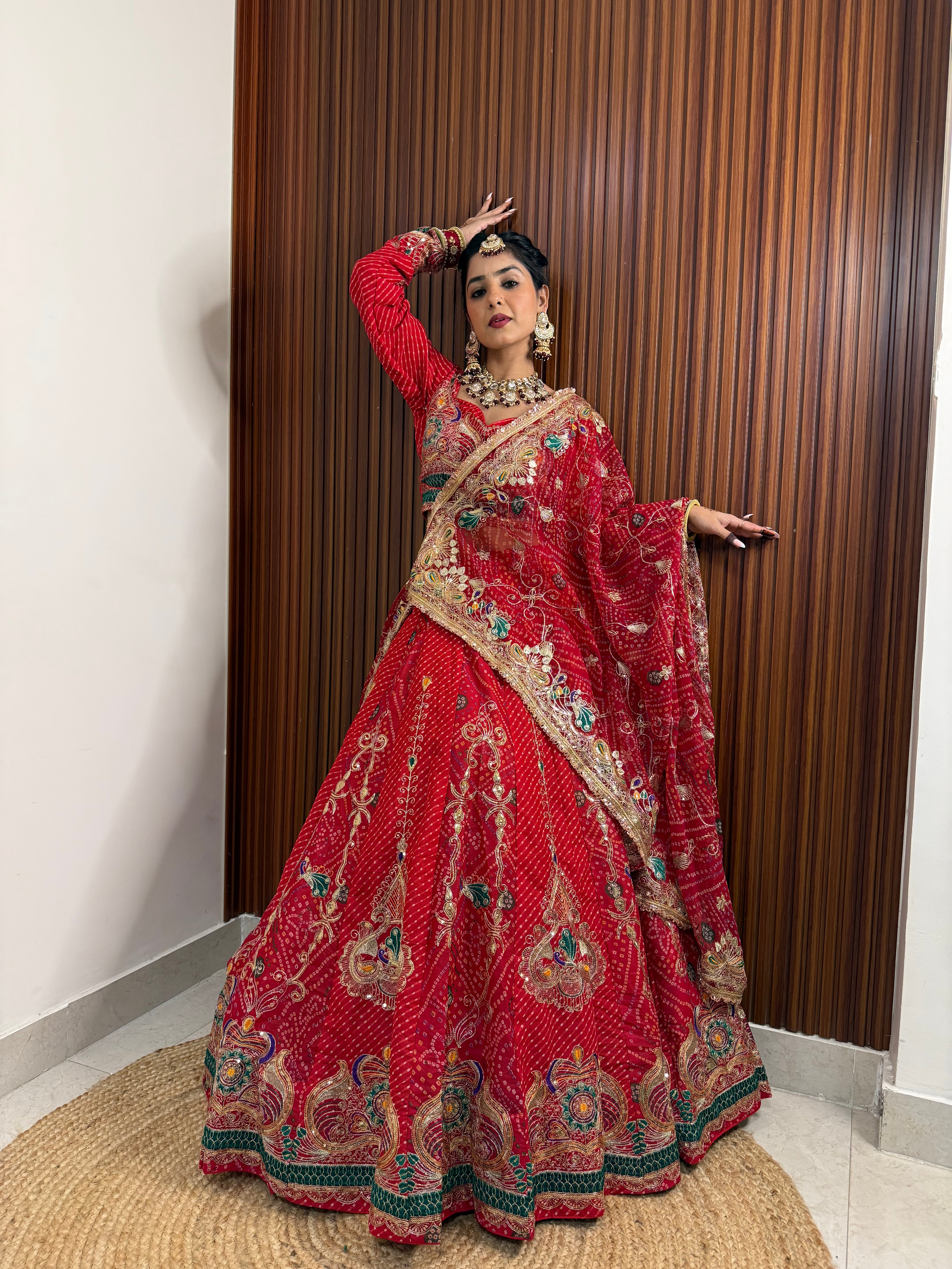 Woman in a traditional red and gold embroidered outfit standing against a wooden paneled wall.