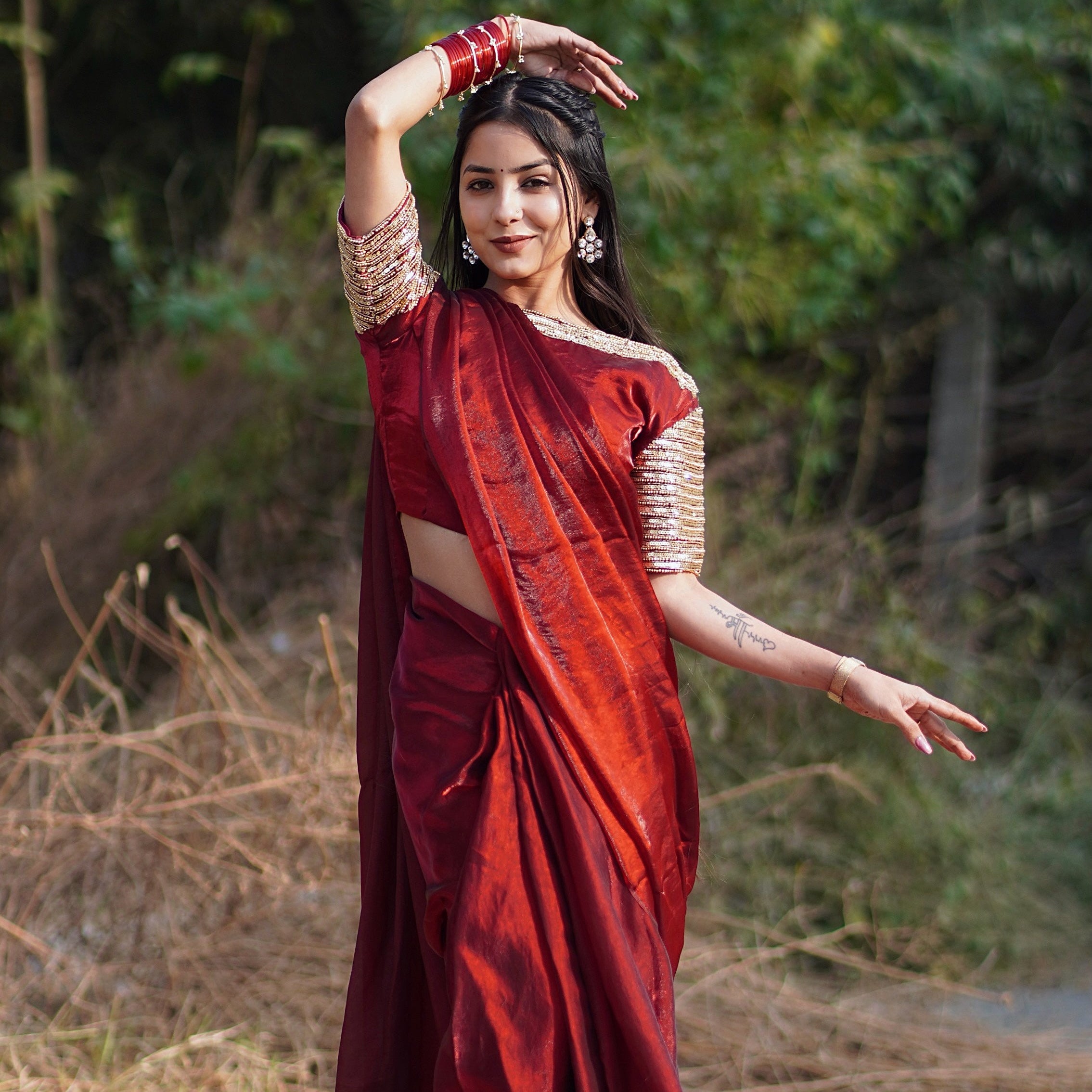 Woman in a red saree standing outdoors with greenery in the background