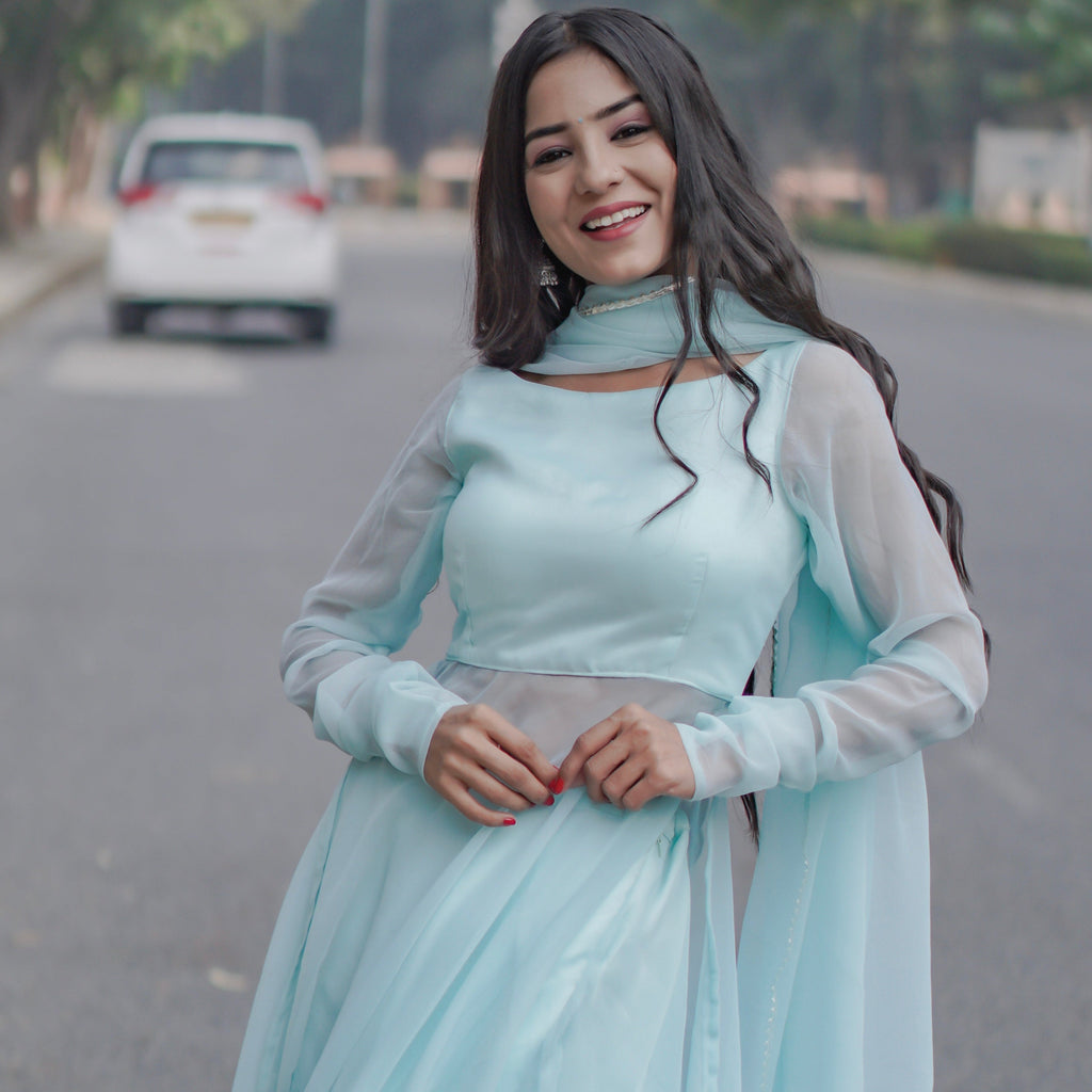 Woman in a light blue dress standing on a road with trees and vehicles in the background