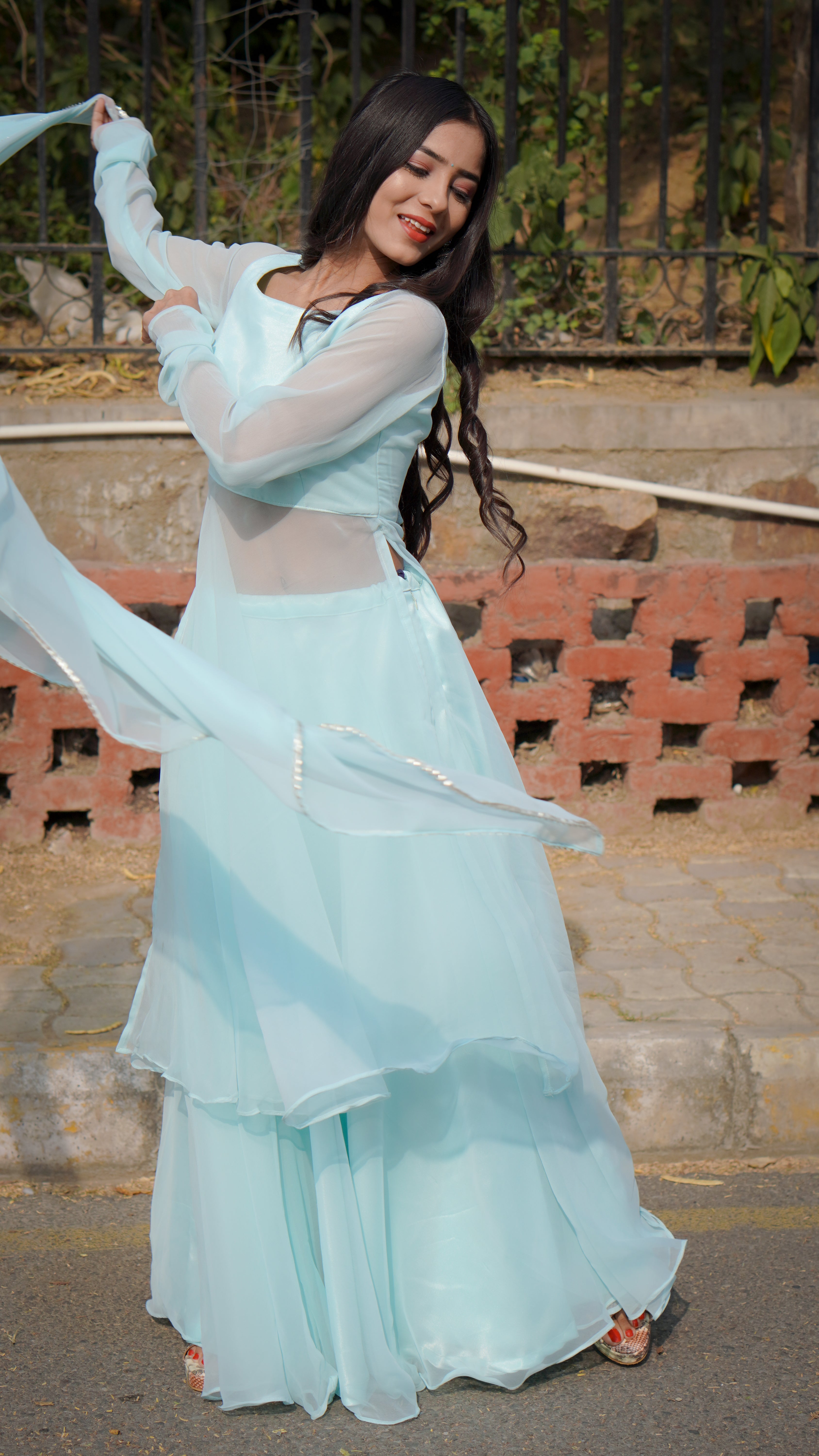 Woman in a light blue dress with sheer sleeves standing outdoors.