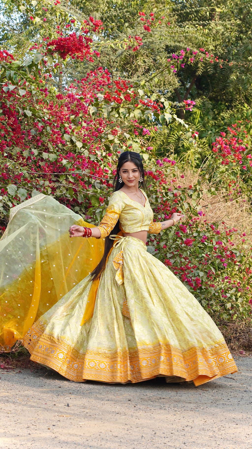 Woman in a yellow traditional outfit standing in front of floral bushes