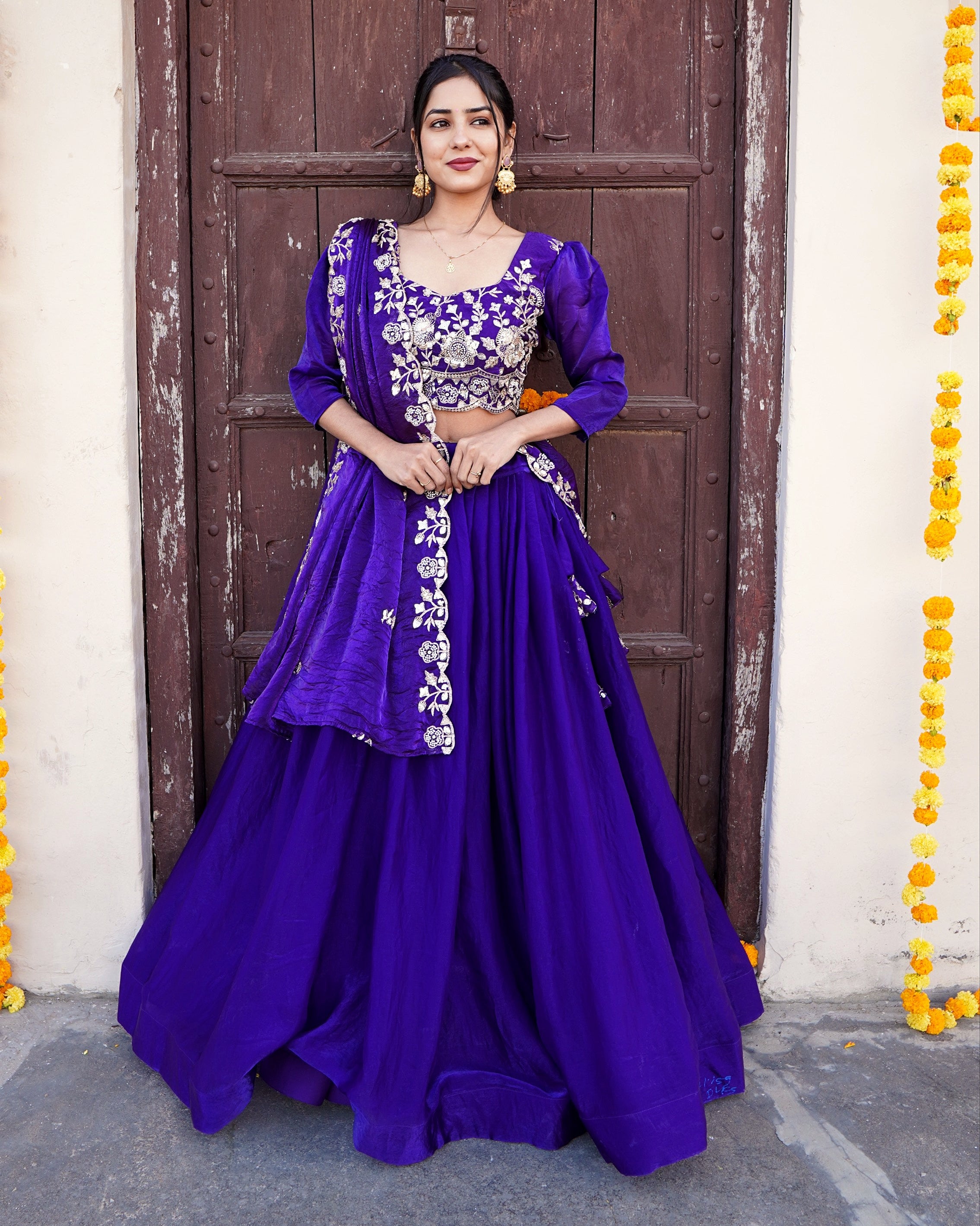 Woman in a purple traditional outfit standing in front of a decorated door.