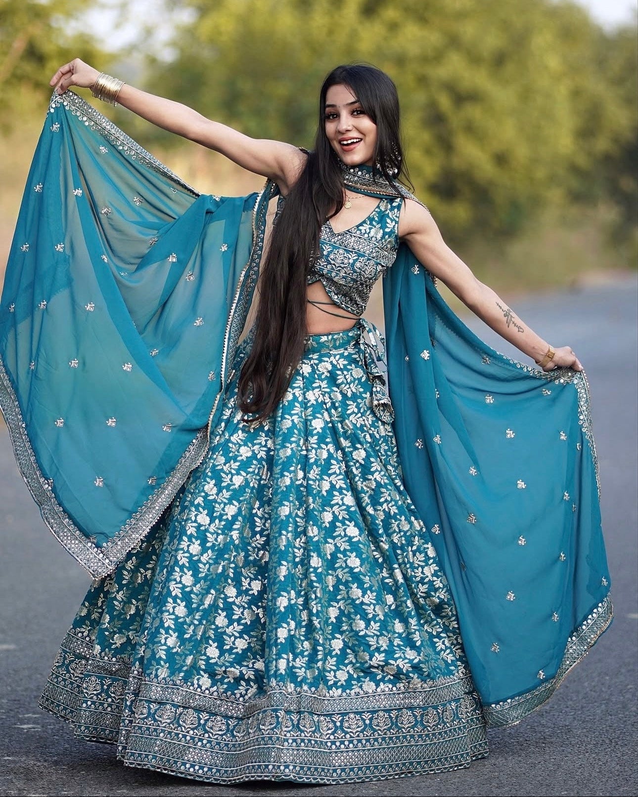 Woman in a blue floral traditional outfit with a dupatta, standing outdoors.