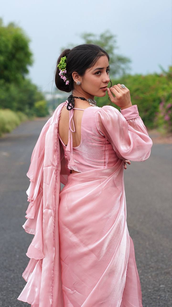 Woman in a pink saree standing on a road with greenery in the background