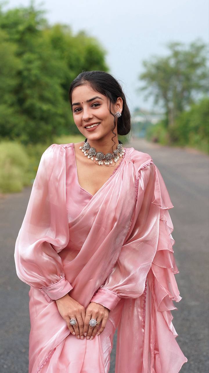 Woman in a pink saree standing on a road with greenery in the background