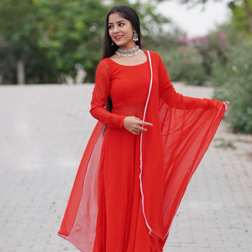 Woman in a red traditional outfit with a long dupatta, standing outdoors.
