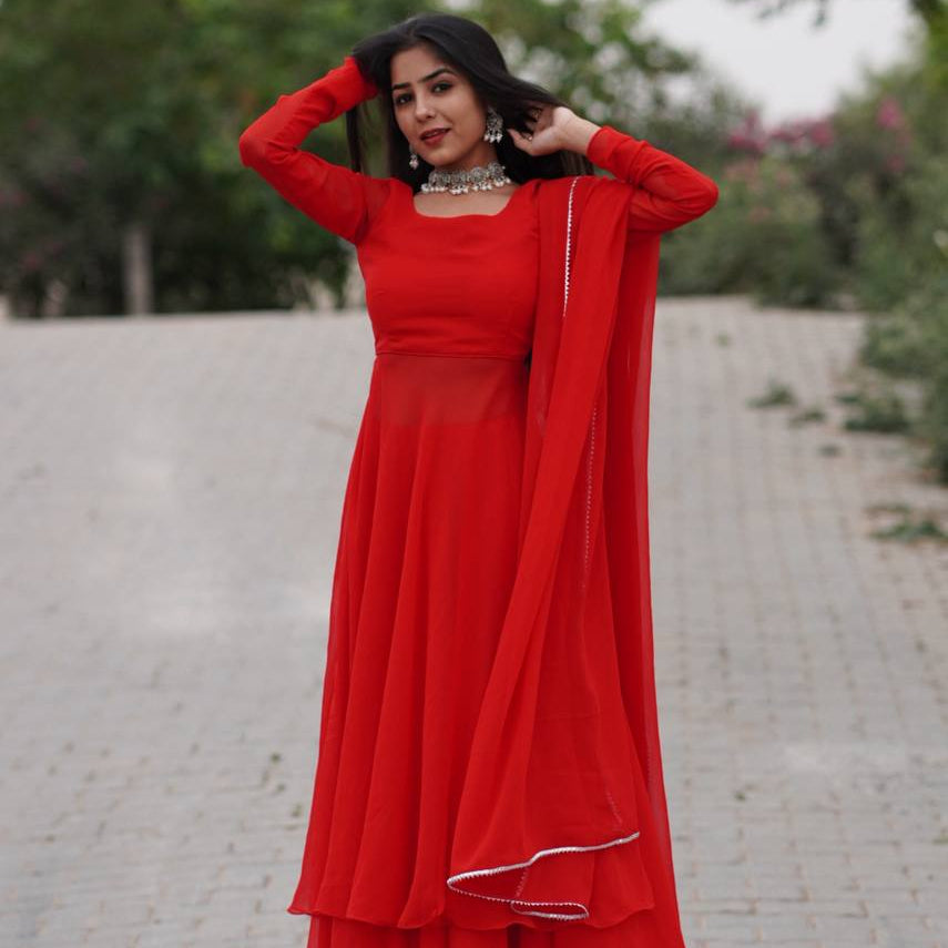 Woman in a red traditional outfit standing outdoors on a paved path with greenery.