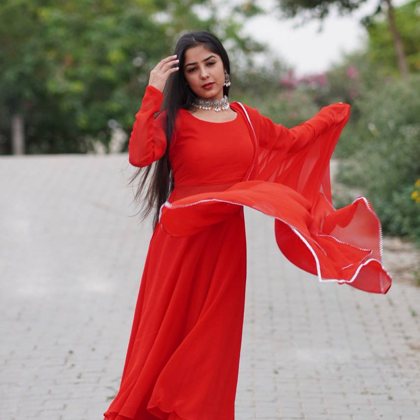 Woman in a red dress standing outdoors with greenery in the background